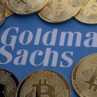 Bitcoin coins surround blurred Goldman Sachs logo