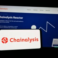 Person holding cellphone with logo of Chainalysis on screen in front of webpage