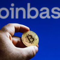 A bitcoin token held in a man’s hands with the Coinbase logo in the background