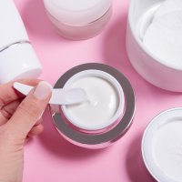 Set of face cream bottles on pink background with a hand holding cosmetic stick
