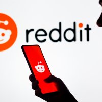 A woman's silhouette holds a smartphone in front of the Reddit logo