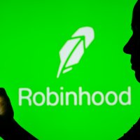 A silhouette holds a smartphone in front of a Robinhood logo