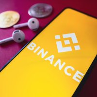 In this photo illustration, the Binance Coin (BNB) logo seen displayed on a smartphone screen, next to two cryptocurrencies and headphones