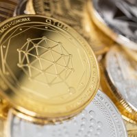 Close up on a gold coin in a pile of coins, designed with the QTUM coin logo