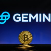 A bitcoin on a stack of coins with Gemini logo on a laptop scree