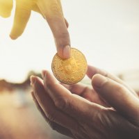 Hand giving bitcoin to a beggar on the street.