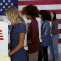 Female voters cast their vote in front of US flag