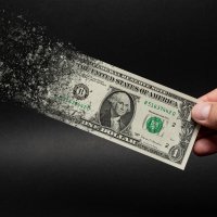 A hand holds a disintegrating one dollar bill 
