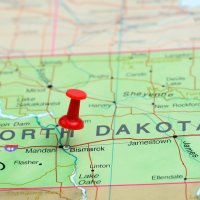 A red pin marks North Dakota on a paper USA map