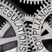 Gear wheels with the words “regulation” and “compliance” written on them – Photo: Shutterstock
