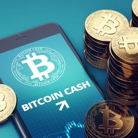 A smartphone screen shows the name Bitcoin Cash surrounded by stacks of bitcoin cash coin