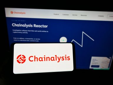 Person holding cellphone with logo of Chainalysis on screen in front of webpage