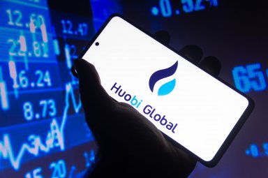 The Huobi logo is seen on a smartphone in front of a market price display