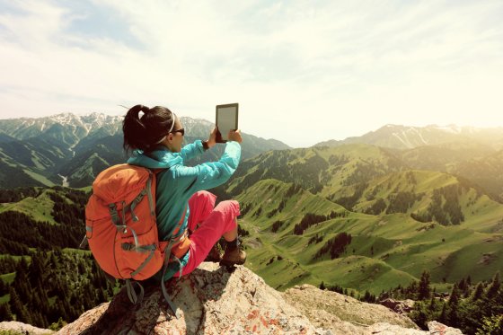 Backpacker atop a mountain with computer tablet
