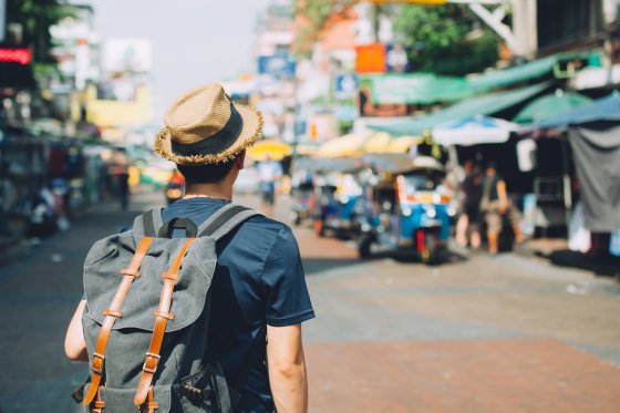 Traveller in T-shirt and straw hat with a backpack walking along a street lined with tuk-tuks