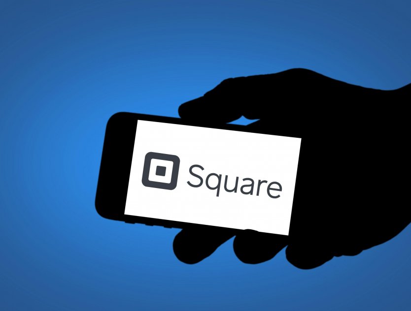 Silhouette of hand holding smartphone that displays Square logo