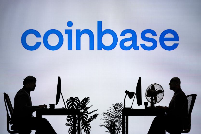 Coinbase logo on an LED screen while two silhouetted people work in an office environment