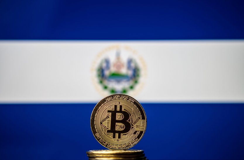 Bitcoin logo represented on a gold coin, stacked in front of the El Salvador flag