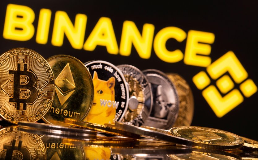 Bitcoin, ethereum, dogecoin, ripple and litecoin coins are displayed seen in front of the Binance company name and logo