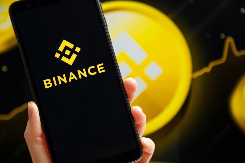 Hand holding mobile with Binance app running at smartphone screen with Binance logo in background