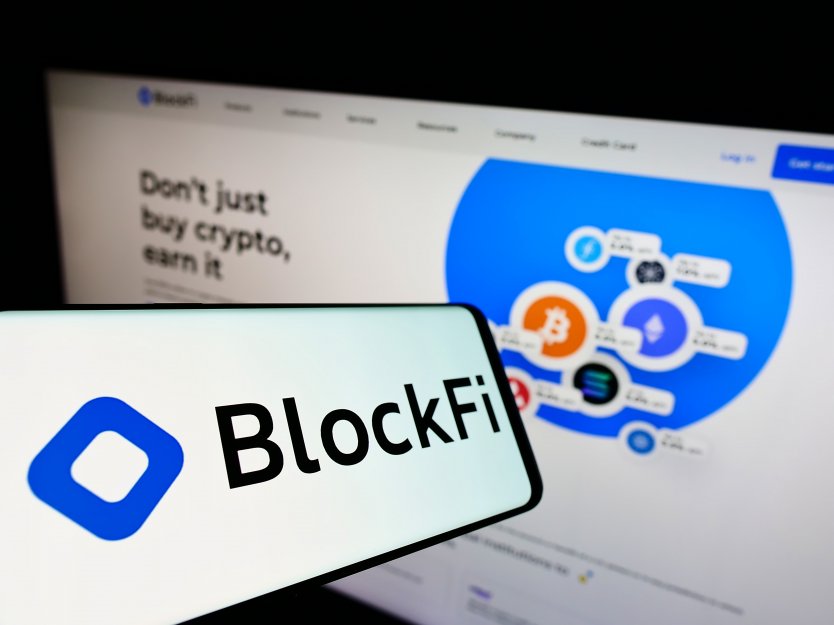 The BlockFi logo on a phone in front of a screen displaying its home page