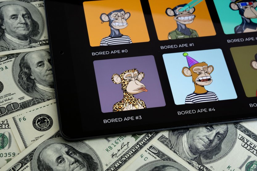 BORED APE NFT digital art collection seen on tablet screen placed on 100 dollar bills