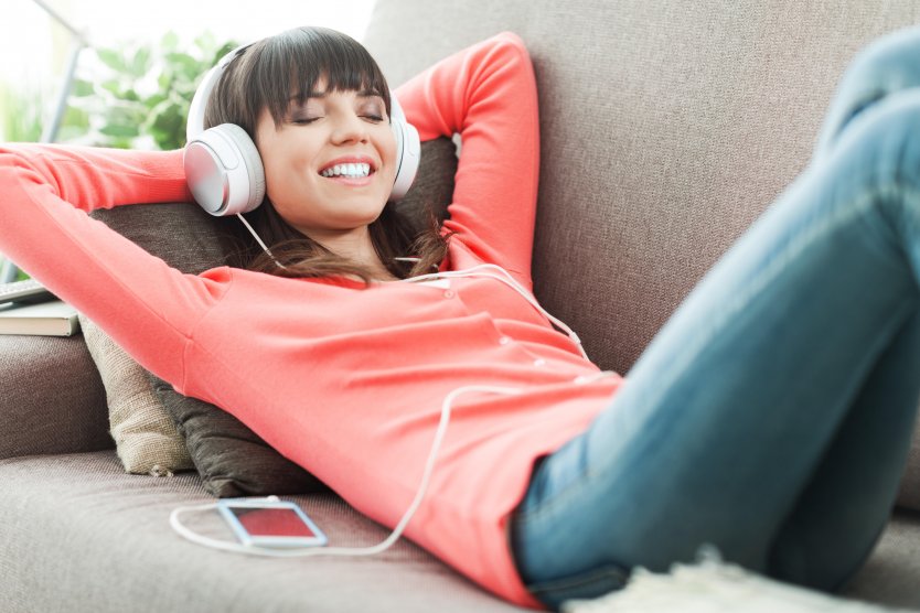 Young woman relaxing on a couch at home, listening to music with headphones