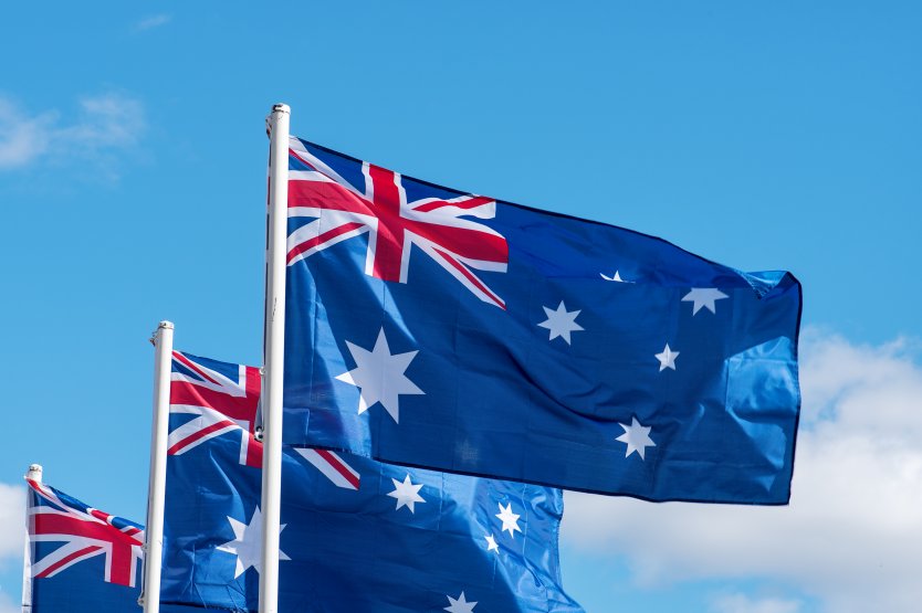 A series of Australian National Flags flutter against a blue sky