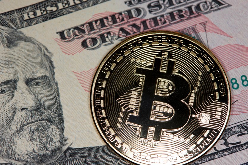 Bitcoin logo represented on a gold coin on top of US dollars in cash notes