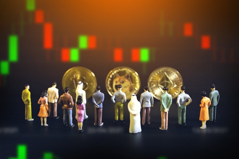 A group of miniature people around physical cryptocurrency coins