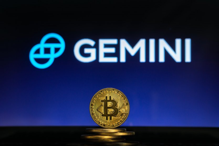 A bitcoin on a stack of coins with Gemini logo on a laptop scree