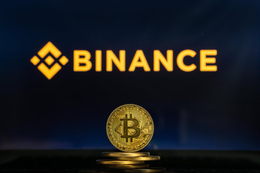 Binance logo on a laptop screen with a stack of bitcoin in the foreground