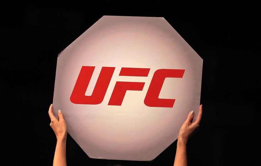 A hands of a ring girl holds aloft a sign that bears the company name UFC