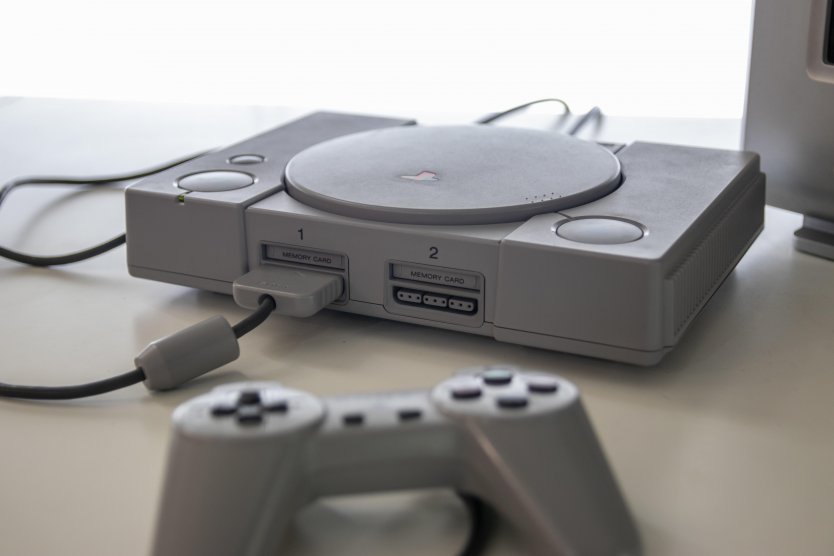 Sony Playstation One and game controller rest on a desk next to a monitor