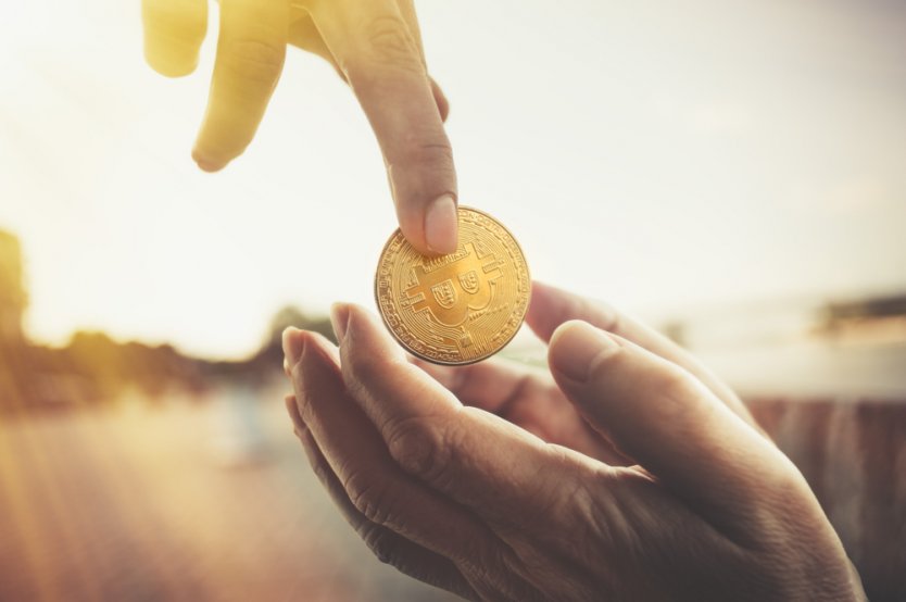 Hand giving bitcoin to a beggar on the street.