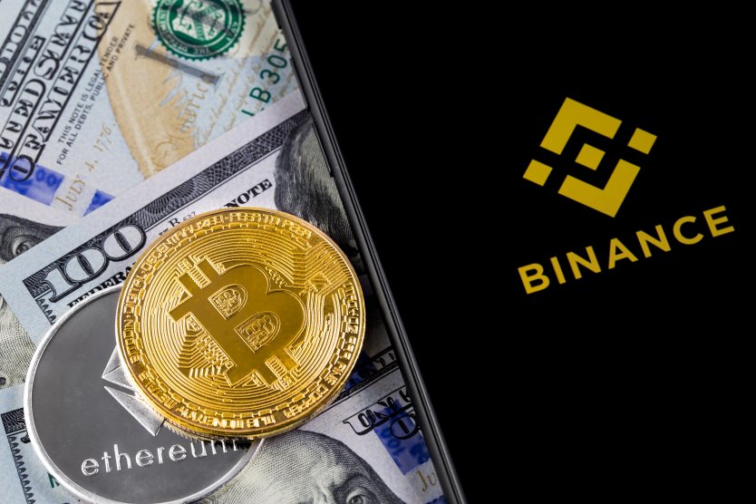 Image showing bitcoin and ethereum tokens on top of currency including USD with a smartphone showing the Binance logo