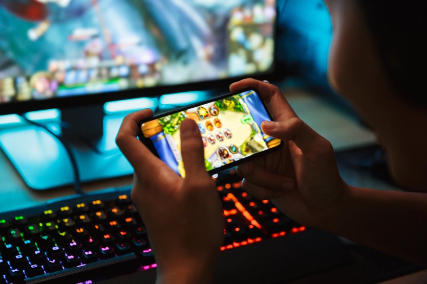 A person at a gaming computer who is also playing a game on a smartphone screen