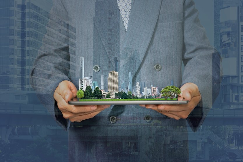 Double exposure with businessman holding tablet and city model in hands