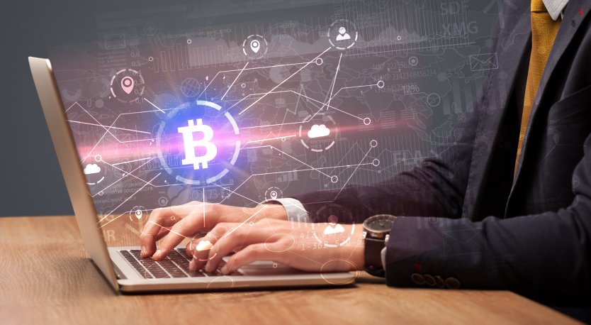 Professional trader working on computer, various icons representing bitcoin, location and cloud computing – Photo: Shutterstock