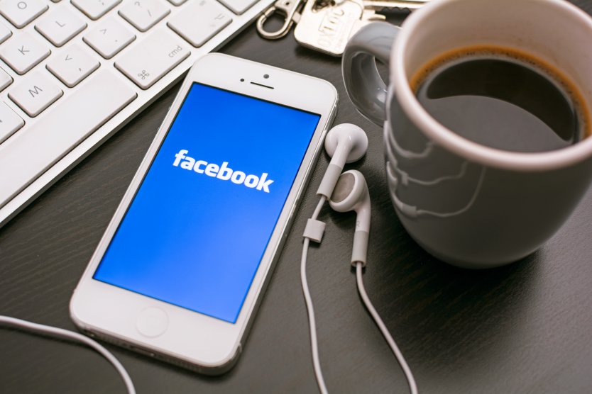 Facebook logo displayed on a mobile phone next to a keyboard and coffee mug