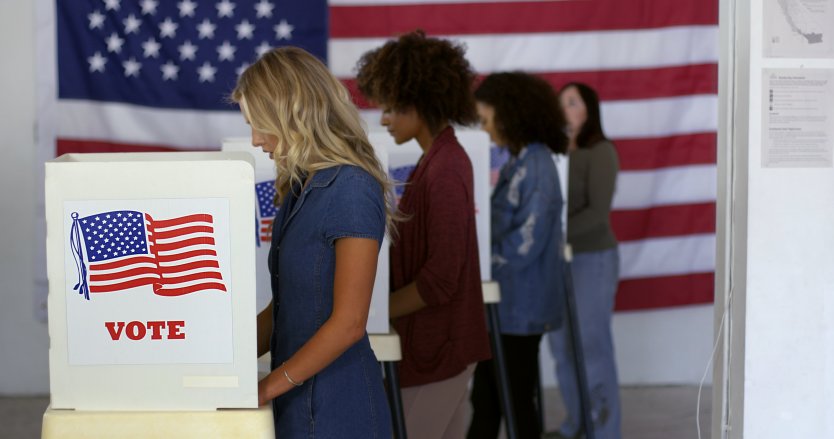 Female voters cast their vote in front of US flag