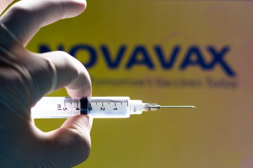 A vaccine syringe with the Novovax logo in the background