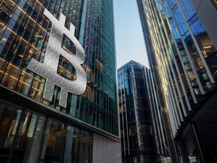 Silver bitcoin symbol on the side of a glass-fronted city building