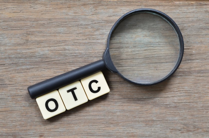 Magnifying glass next to Scrabble letters O T and C on wooden desk surface – Photo: Shutterstock