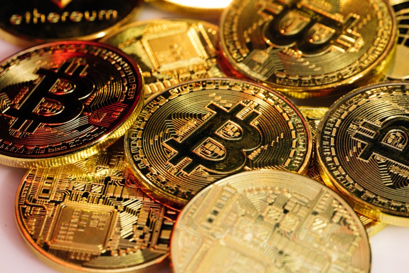 A pile of bitcoin tokens lie on top of other golden coins that resemble a computer’s motherboard