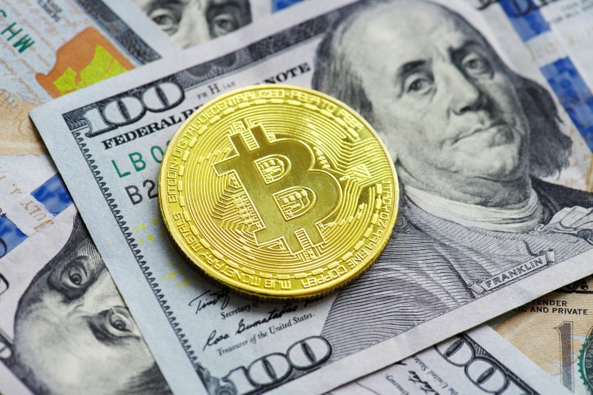 Representation of a golden bitcoin lying flat on a $100 bill