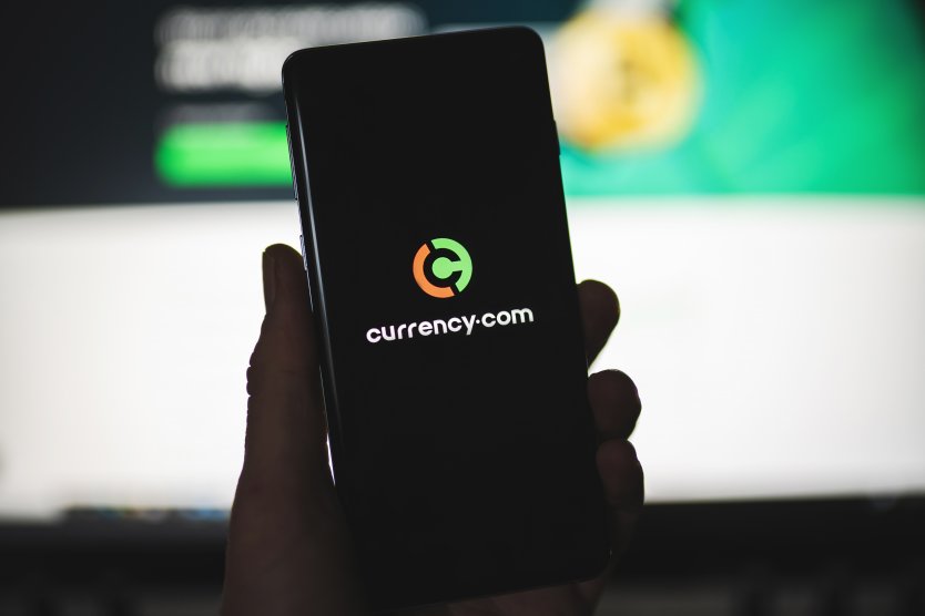 Smartphone with Currency.com logo with blurred website as background. Trading platform, stocks and cryptocurrencies. SWANSEA, UK - MARCH 12, 2021