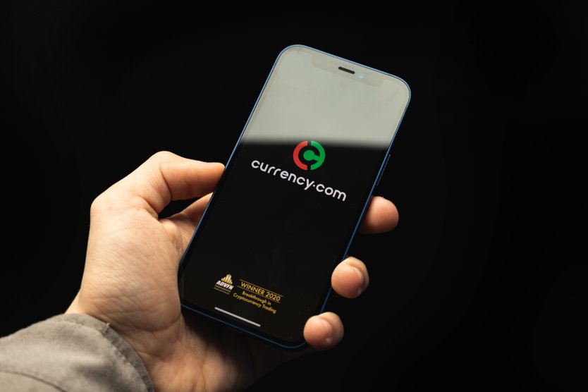 Currency.com expands into the US with new crypto exchange services Crypto exchange currency.com app logo on the screen, man use application for buying and sold bitcoin and other cryptocurrency, black background photo