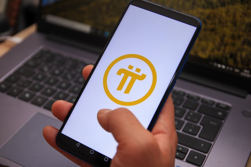 Hand holding a smartphone bearing the Pi Network logo