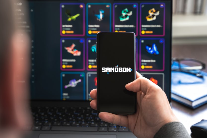 The Sandbox logo seen on a mobile phone in front of a gaming screen